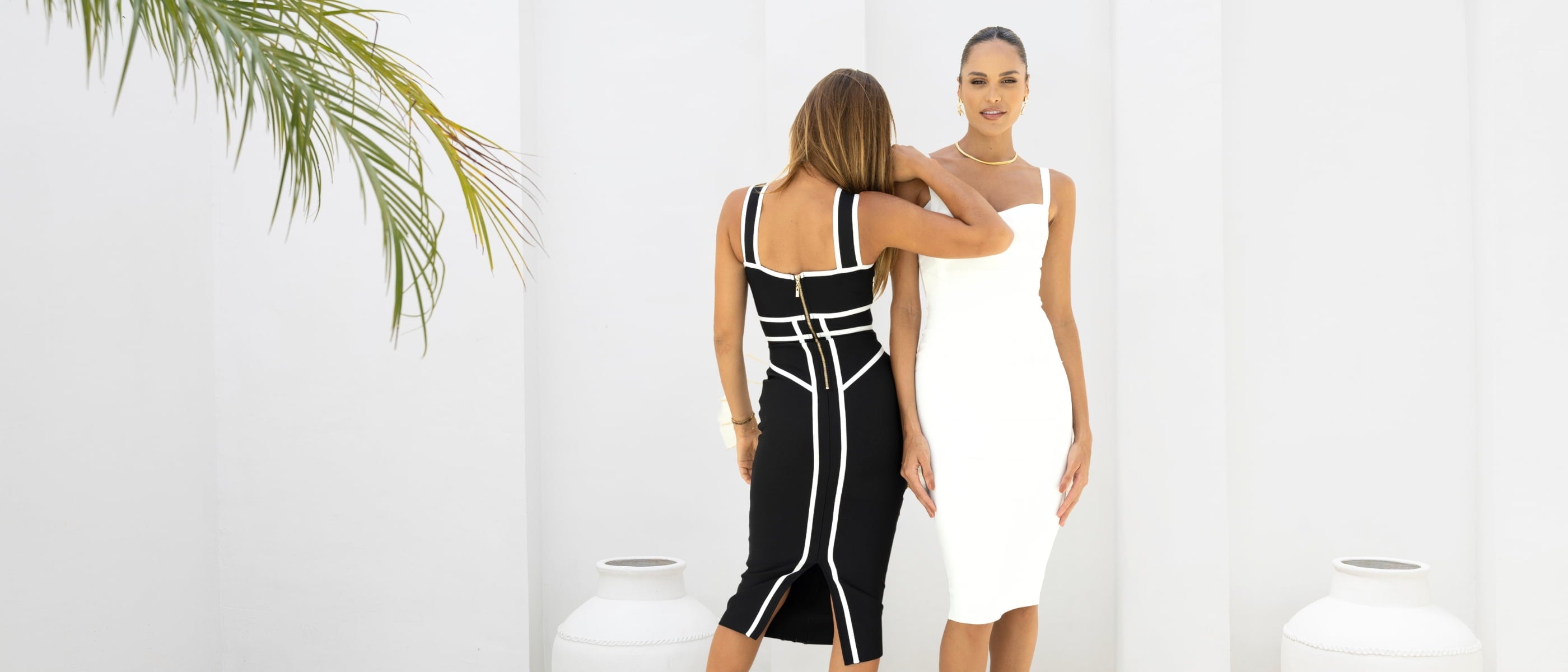 Two women wearing black and white bodycon party dresses against a white background.
